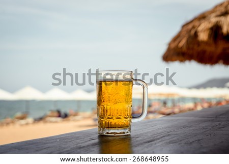 Mug of cold beer with foam on the table. Against the background of the sea. The Restaurant