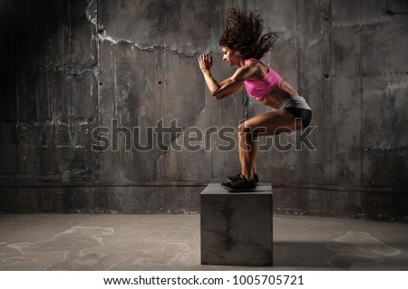 Fit young woman box jumping at a crossfit style on gray background. Fitness,  functional, training, and lifestyle concept