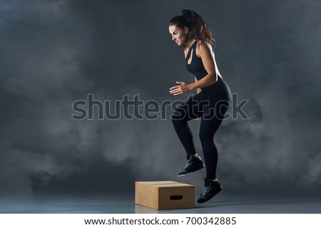 Fit young woman box jumping at a crossfit style on gray background with copy space. Fitness, crossfit, functional, training, and lifestyle concept