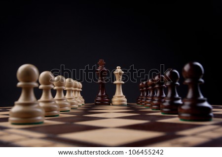 black king and white queen with chess pieces on both sides on a chess board; dark background