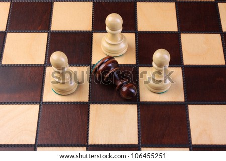 One black chess piece surrounded by three white chess pieces on a chess board