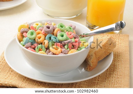 A bowl of colorful fruit flavored breakfast cereal with orange juice