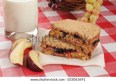 A peanut butter and jelly sandwich with apple slices and milk