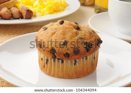 A chocolate chip muffin with sausage and eggs in the background