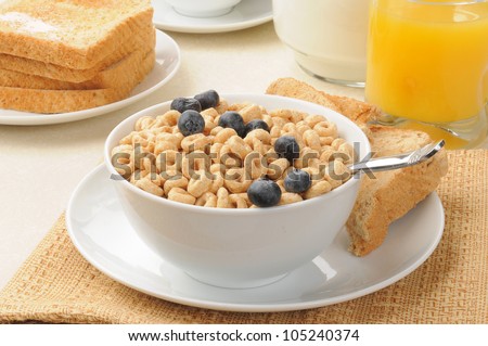 A bowl of oat breakfast cereal with blueberries, toast and orange juice