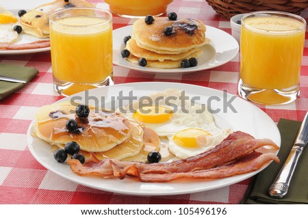 A breakfast with bacon and fried eggs with blueberry pancakes and orange juice