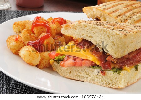 A bacon, lettuce and tomato panini with cheese and hash brown puffs