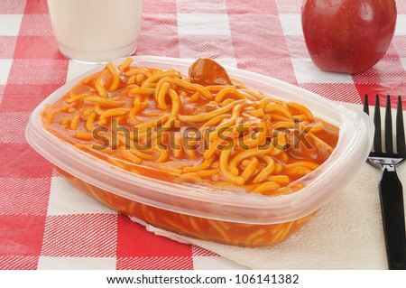 A packed lunch with microwave spaghetti an apple and milk