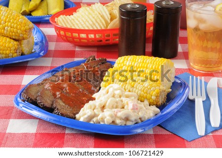 Picnic lunch with barbecue beef brisket with corn on the cob and macaroni salad