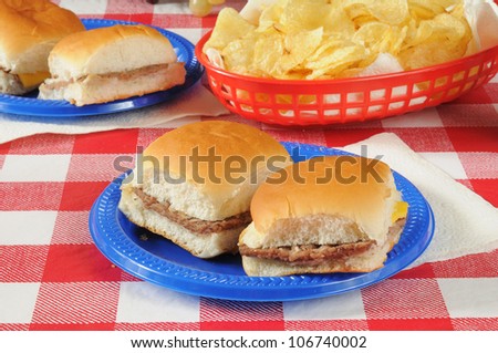 A plate of sliders or mini cheeseburgers on a picnic table with potato chips
