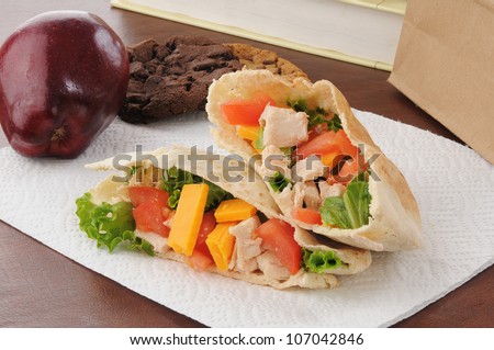 a healthy school or sack lunch with a chicken pita sandwich, apple and cookies