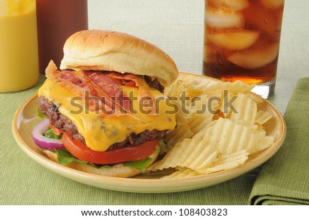 A bacon cheeseburger with potato chips and a cola
