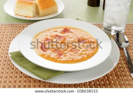 A bowl of bean and bacon soup with dinner rolls