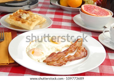 A big breakfast with bacon, eggs, waffles, and pink grapefruit