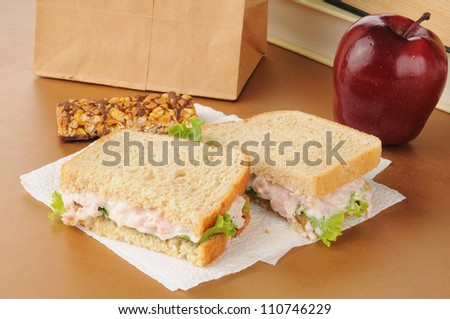 A school lunch with a deviled ham sandwich, apple, granola bar and textbooks