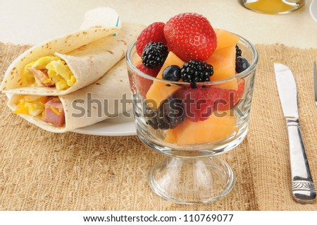A cup of berries and cantaloupe with breakfast burritos