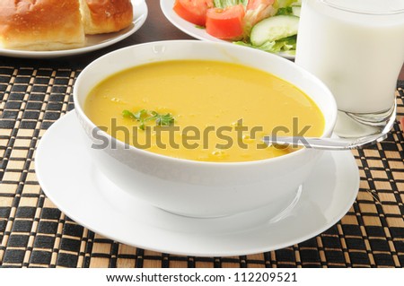 A bowl of organic butternut squash soup with a salad and dinner rolls