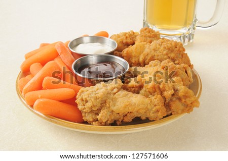 A snack plate with chicken wings and carrots sticks and a mug of beer