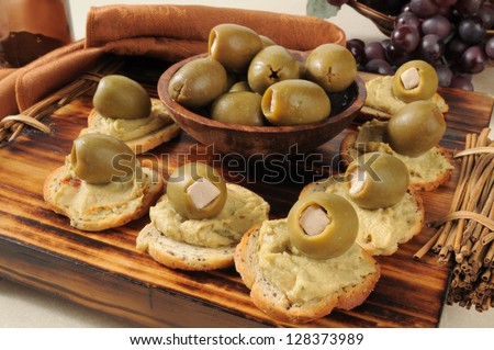 Spinach artichoke hummus on bagel toasts topped with greek olives stuffed with feta cheese