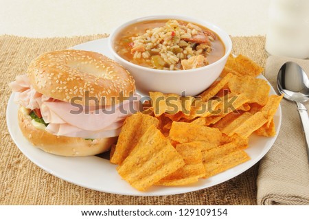 A ham sandwich on a bagel with chicken sausage gumbo and natural chips