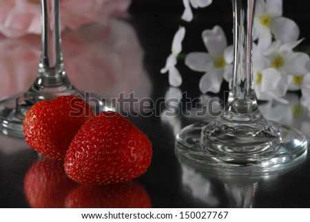 Roses, white flowers, wine glasses and strawberries reflect on a glass table