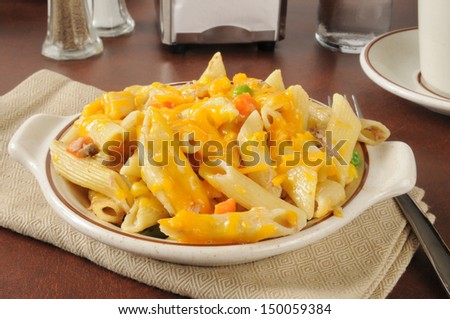 A bowl of tuna casserole on penne pasta topped with grated cheddar cheese
