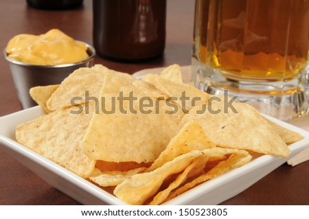 Closeup of tortilla chips with cheese sauce and beer - shallow depth of filed, focus on chips in front