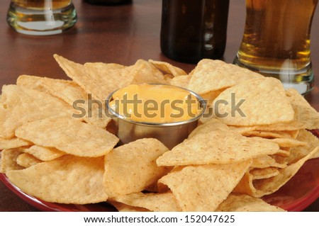 A plate of tortilla chips and cheese sauce and a glass of beer