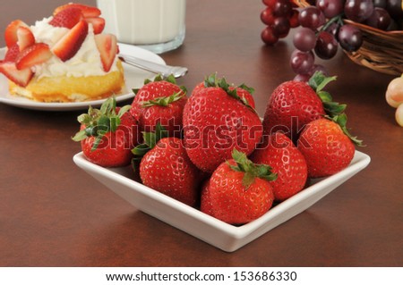 A bowl of fresh strawberries with strawberry shortcake and milk in the background - focus on bowl of strawberries