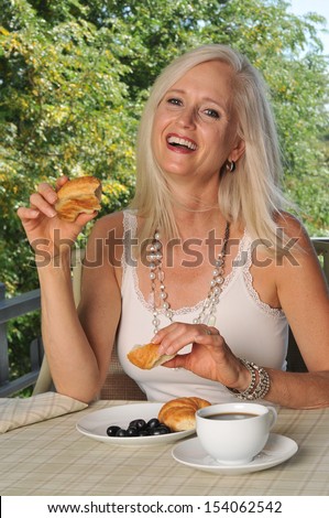 A happy mature woman enjoying coffee and a croissant on the patio