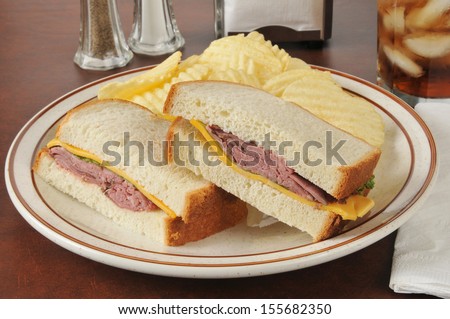 A roast beef and cheddar cheese sandwich with potato chips and a soft drink