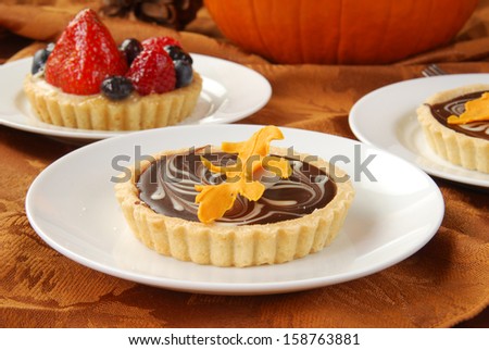 Chocolate and fruit dessert tarts on a holiday dessert buffet with a pumpkin