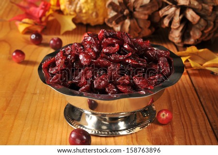 A silver serving dish of dried cranberries in an autumn setting