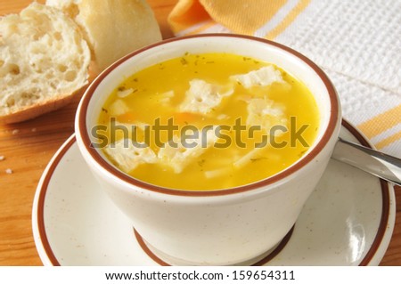 A cup of chicken noodle soup with a broken open roll