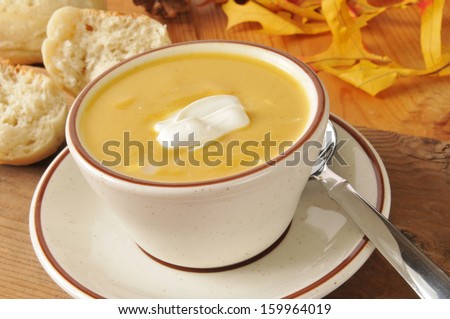 A cup of butternut squash soup with a dinner roll on a rustic wooden table
