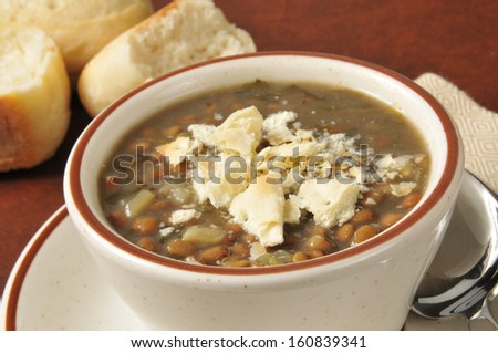 A cup of lentil soup with saltine crackers and dinner rolls in the background