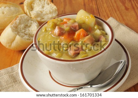A cup of split pea soup with a dinner roll