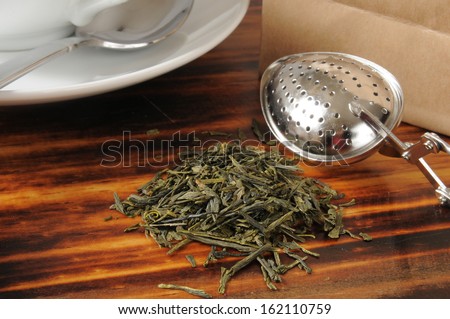 Whole leaf green tea on a counter with a tea infuser and the bag it came out of