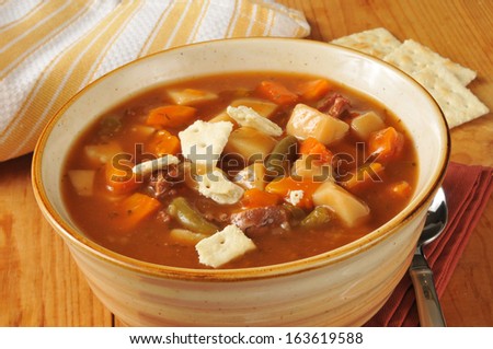 A bowl of vegetable beef soup with saltine crackers on rustic wooden table