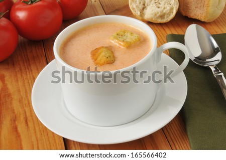 a cup of cream of tomato soup with dinner rolls