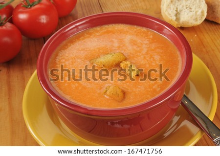 A bowl of creamy tomato soup with dinner rolls