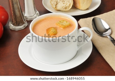 A cup of tomato soup with croutons and dinner rolls