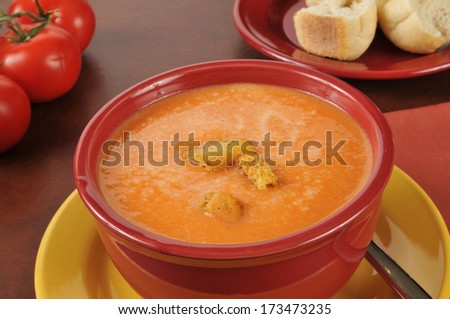 a bowl of creamy tomato soup with hard rolls and croutons