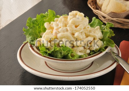 A small bowl of macaroni salad with dinner rolls
