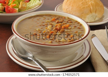 A bowl of lentil soup with a dinner roll and salad