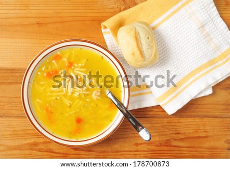 A bowl of chicken noodle soup with a dinner roll