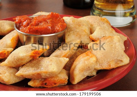 Closeup of a plate of pizza rolls with marinara sauce and beer in the background