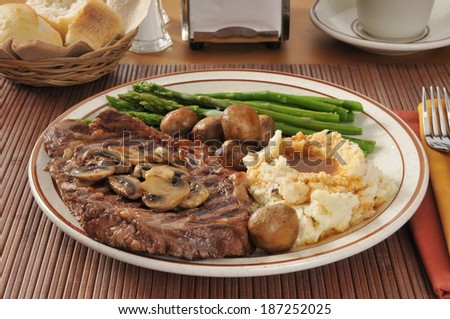 A grilled rib steak with sauteed mushrooms, asparagus, and mashed potatoes