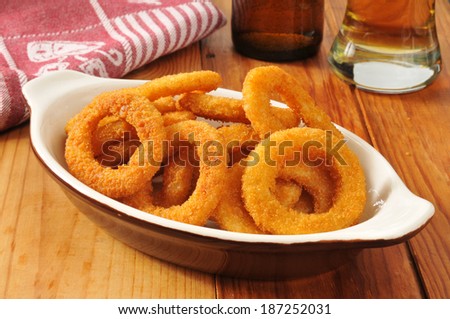 A serving of golden onion rings with beer on a rustic wooden bar counter