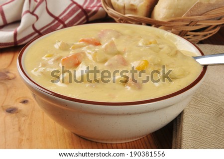 A bowl of hearty chicken corn chowder with a basket of dinner rolls